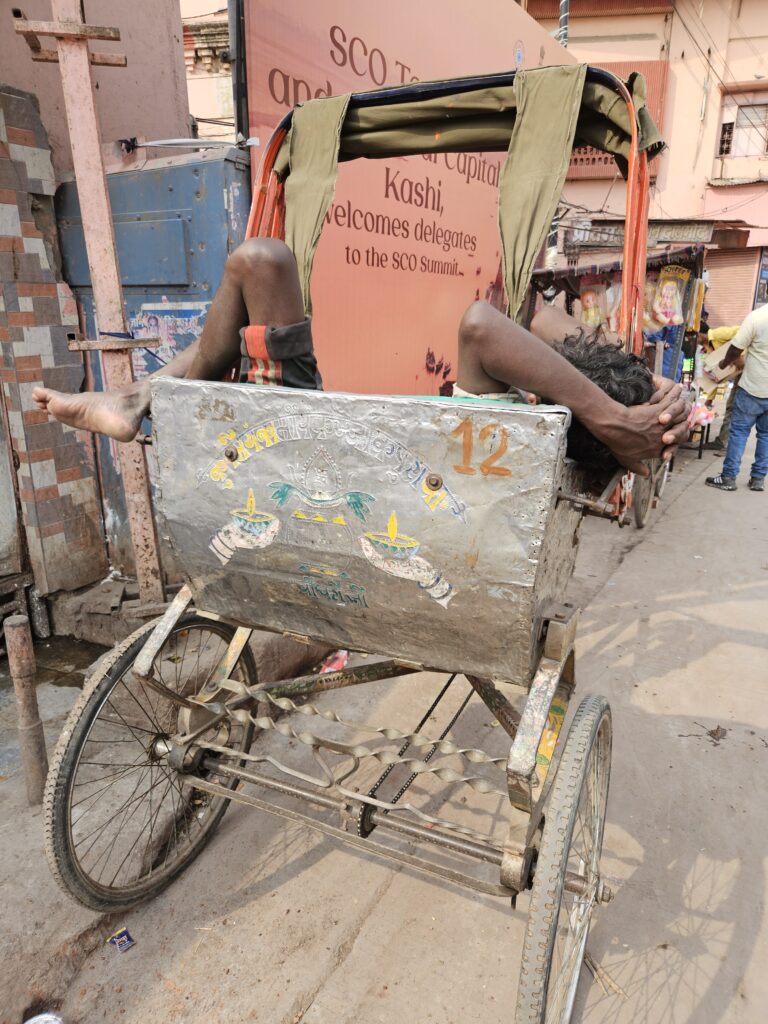 Riksjadriver rust uit liggend in zijn fietsriksja op straat in Varanasi, India.