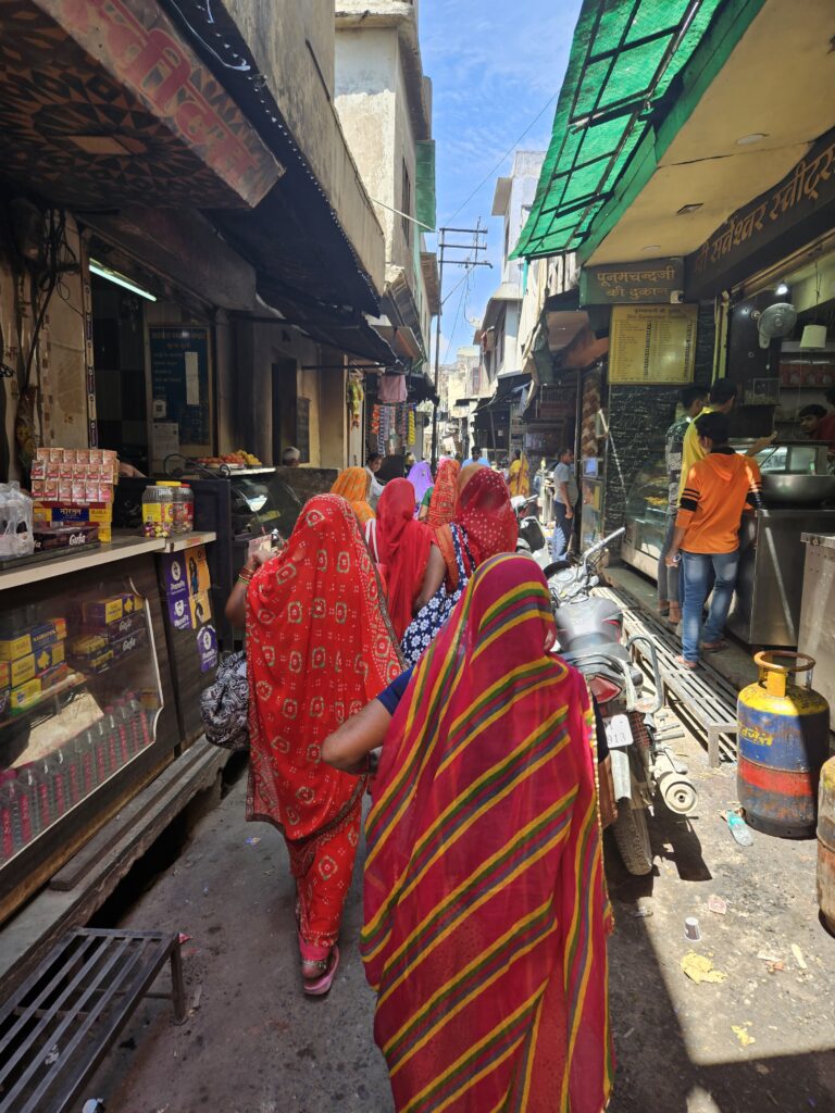 Vrouwen in kleurrijke sari’s lopen door een smalle marktstraat in Pushkar, Rajasthan.