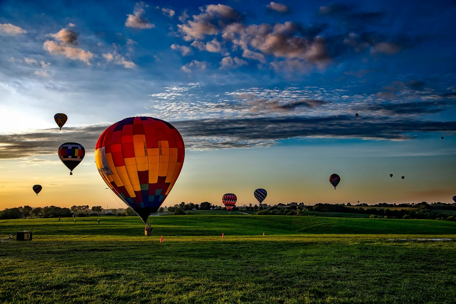 Vibrant hot air balloons take off at dawn over a rural field, showcasing a picturesque landscape.