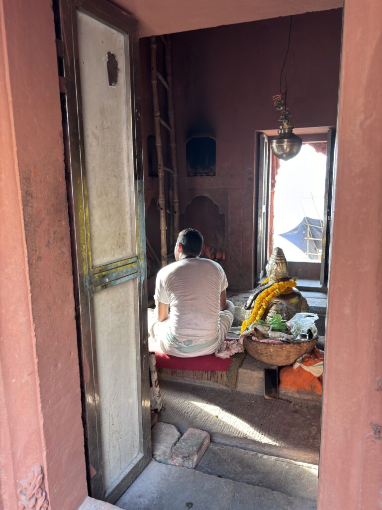 Priester in witte dhoti bidt voor een Shiva-lingam in een kleine tempel in Varanasi.