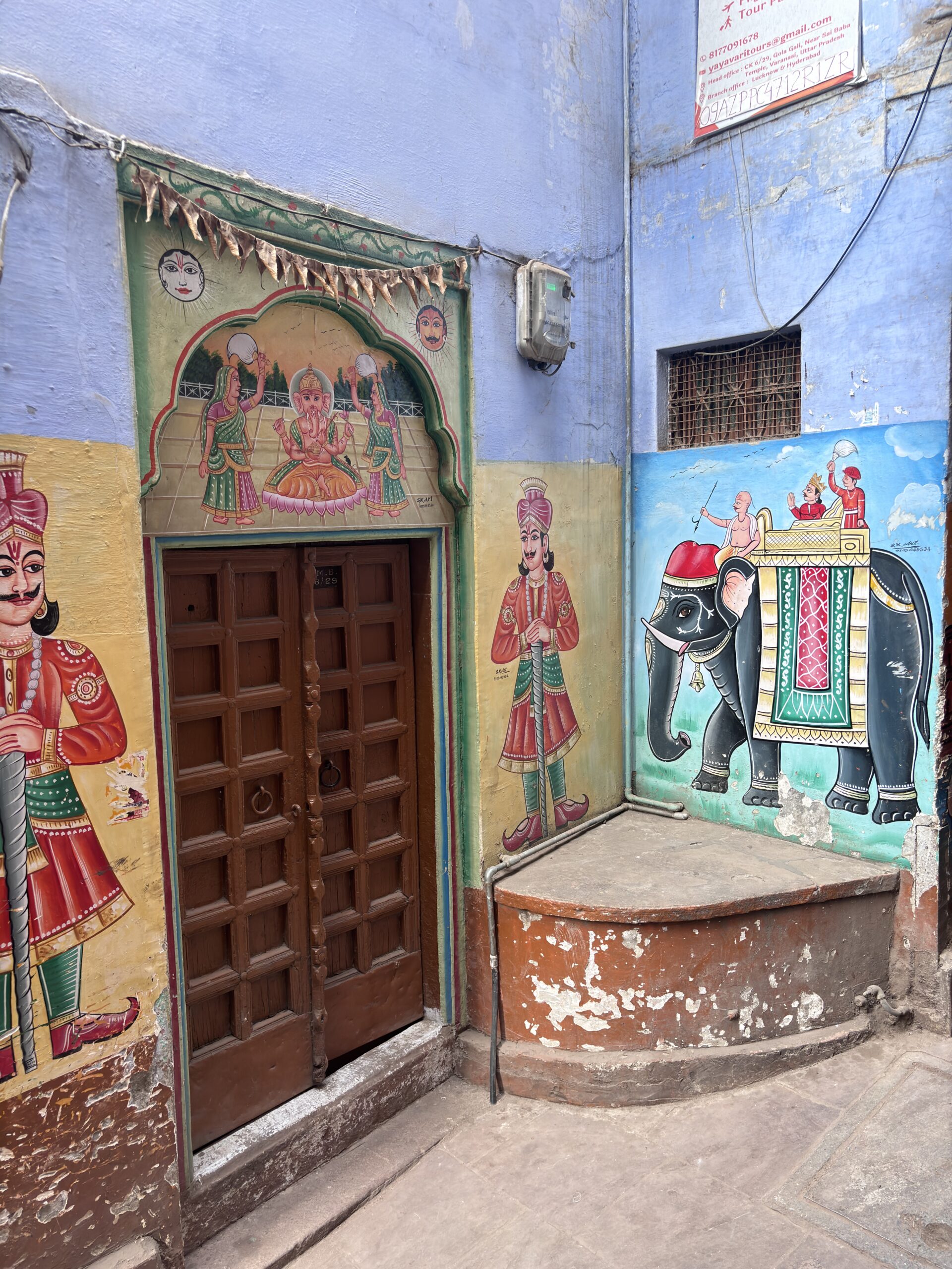 Muurschilderingen van hindoegoden, krijgers en een olifant bij een huisdeur in een steeg in Varanasi, India.
