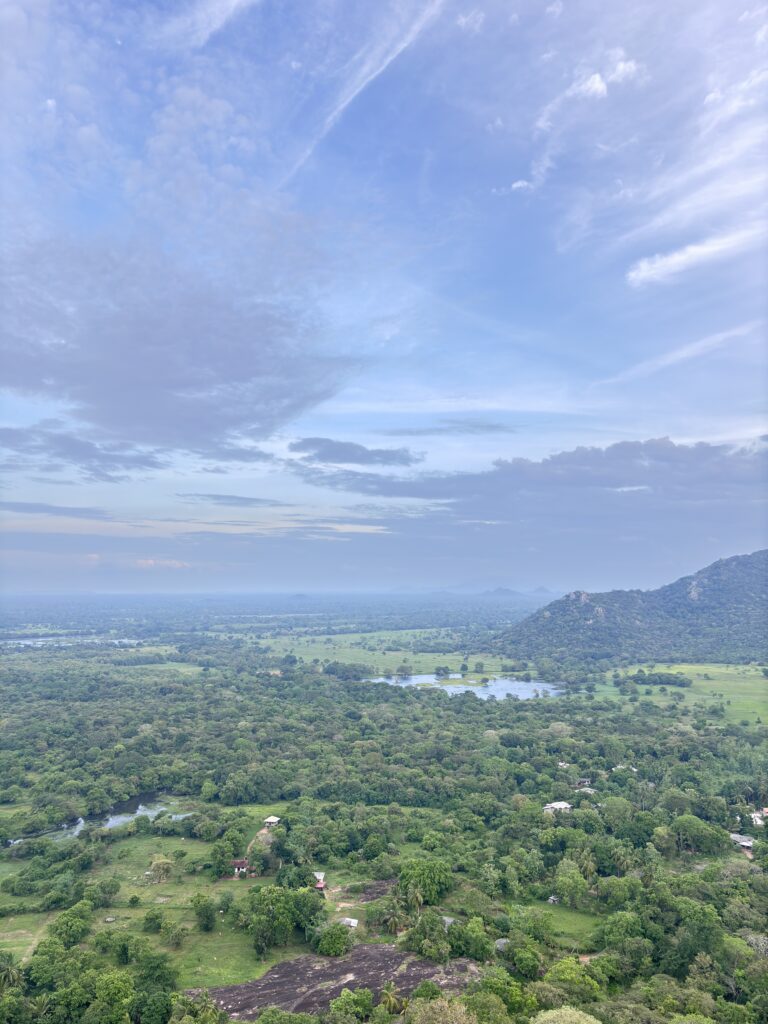 Uitzicht over een groene vallei met bossen, meren en heuvels onder een blauwe lucht met wolken.