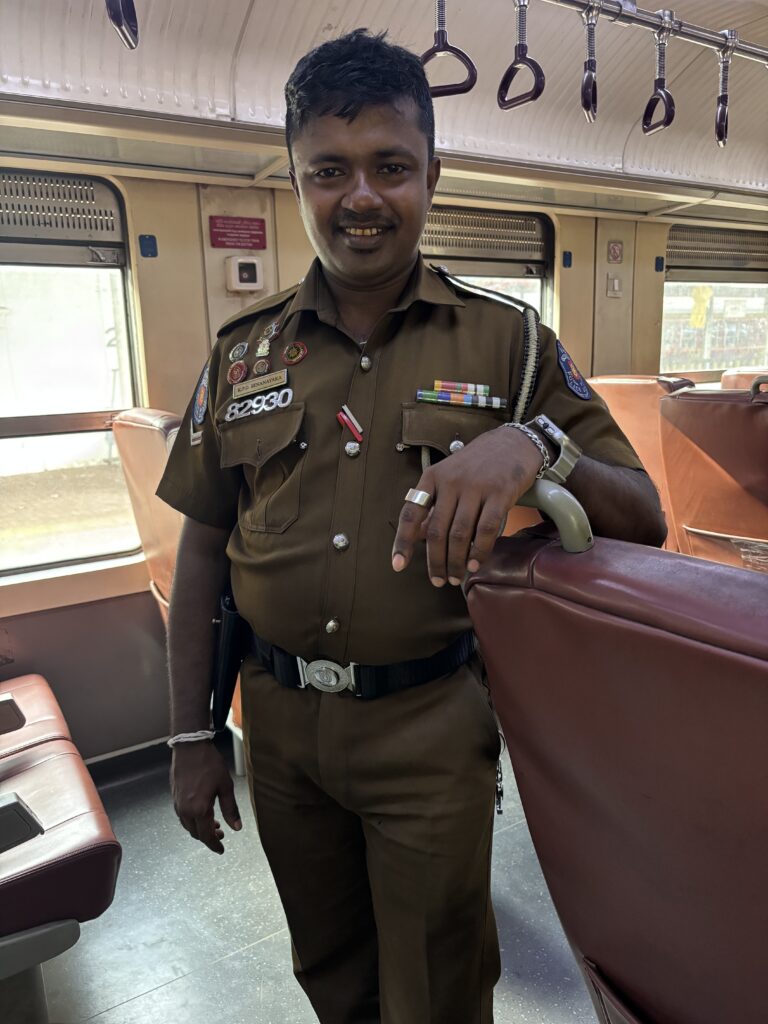 Man in bruin uniform met medailles en insignes poseert glimlachend in een treinwagon.