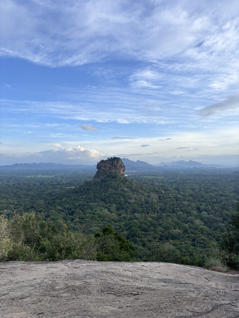 Uitzicht op de iconische Sigiriya Leeuwenrots in Sri Lanka, omringd door dicht groen woud en blauwe lucht.