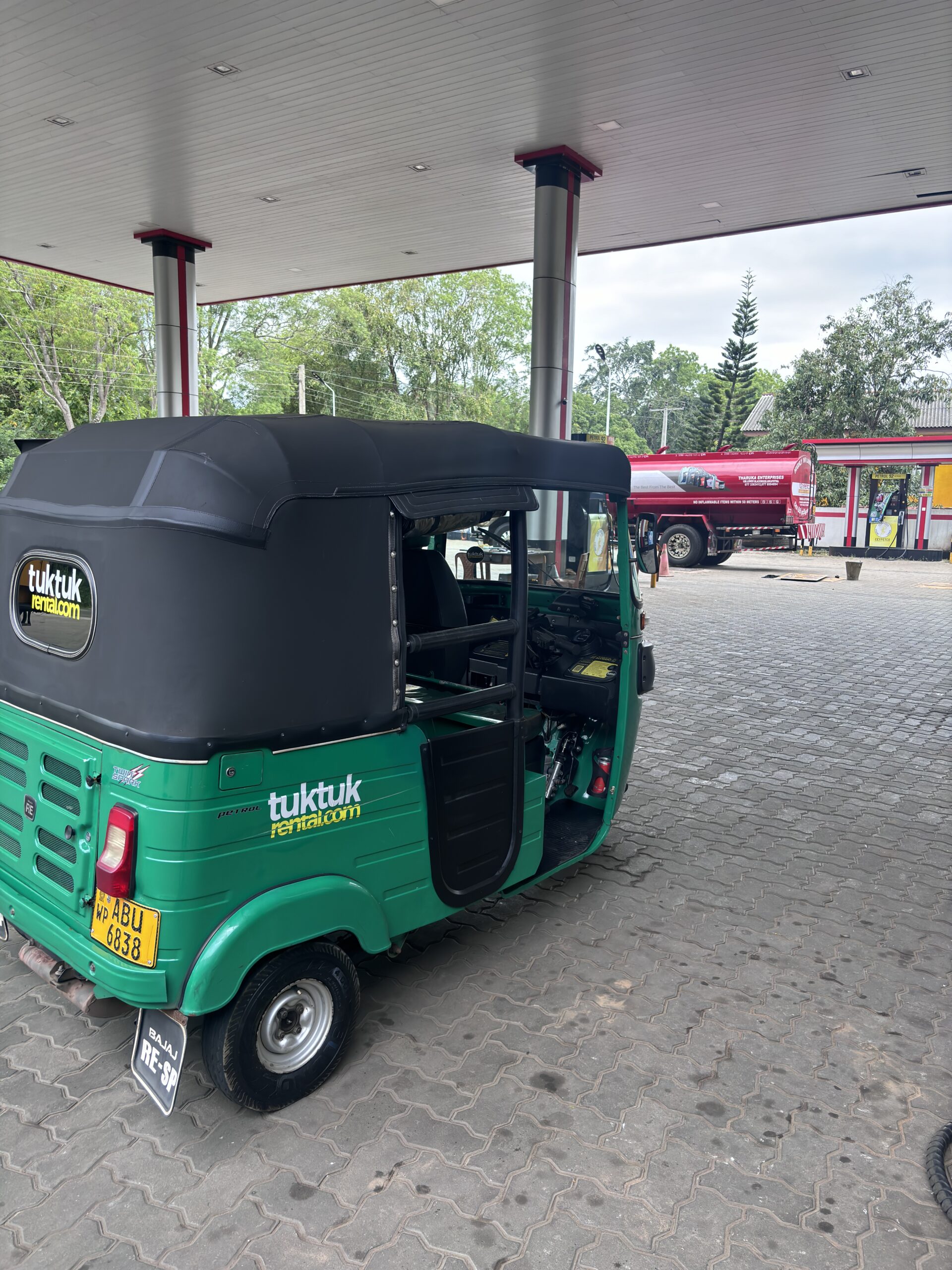 Groene tuktuk van TukTukRental.com geparkeerd bij een tankstation in Sri Lanka