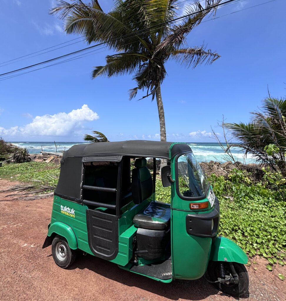Groene tuk tuk geparkeerd langs een kustweg met palmbomen en uitzicht op de oceaan. Tuktukrental.