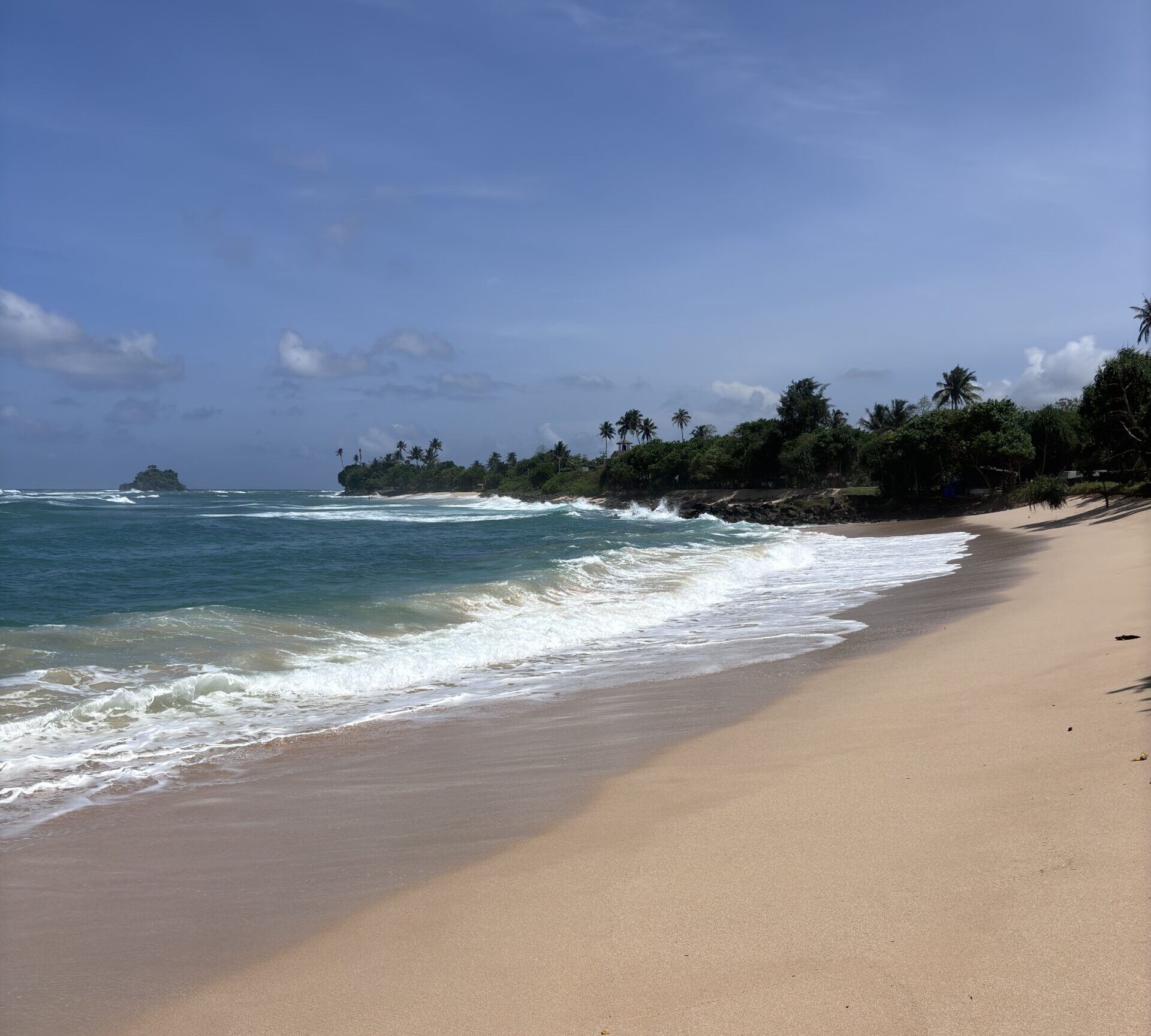 Tropisch strand met helderblauwe zee, palmbomen en golven die op het zand breken in Sri Lanka.