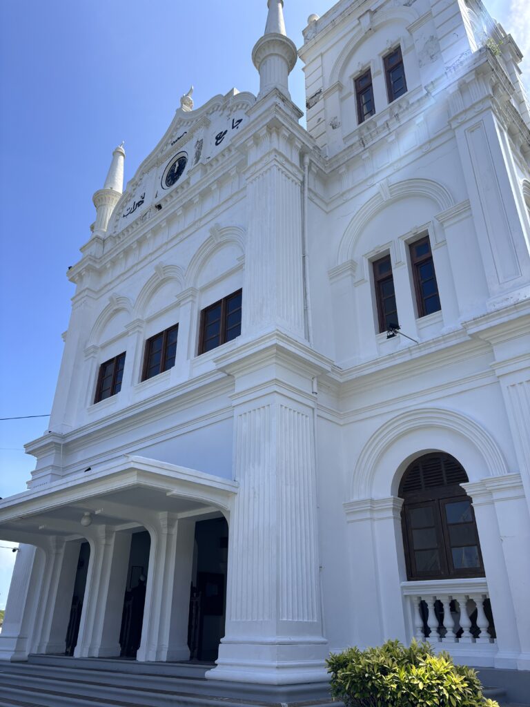 Witte moskee in Galle met hoge zuilen, torens en een klok tegen een helderblauwe lucht.