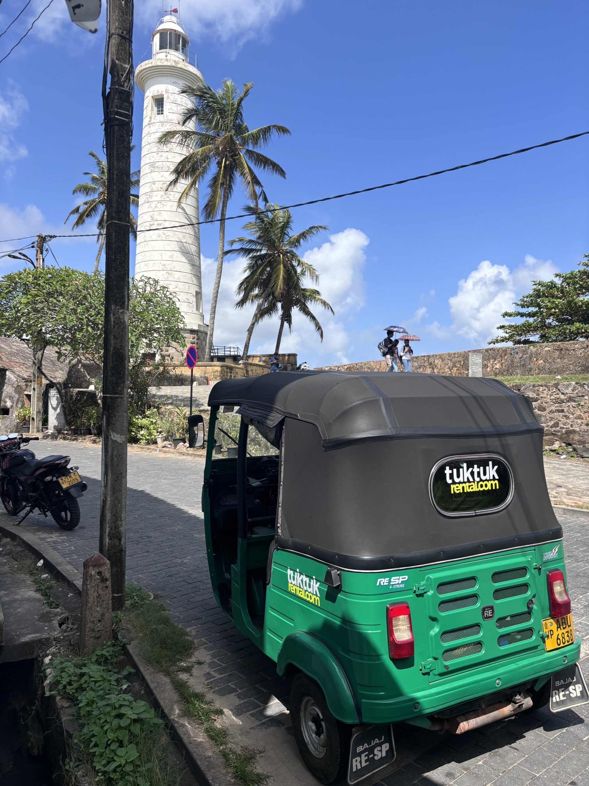 Groene tuktuk voor de vuurtoren van Galle Fort in Sri Lanka met palmbomen en blauwe lucht.